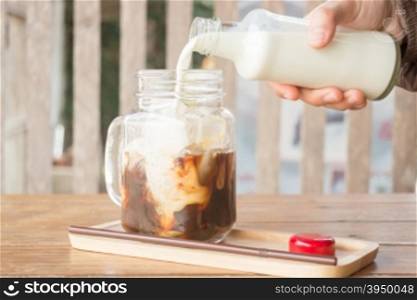 Pouring milk to iced glass of coffee, stock photo