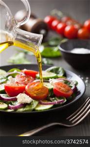 pouring olive oil on salad with tomato and cucumber