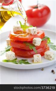 pouring olive oil over salad with beef tomatoes and feta