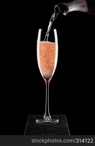 Pouring pink rose champagne from bottle to glass on black marble board on black background.
