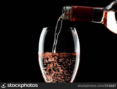 Pouring pink rose wine from bottle to glass isolated on black background