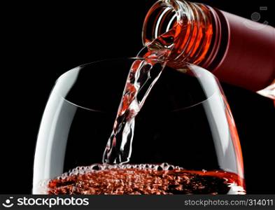 Pouring pink rose wine from bottle to glass isolated on black background