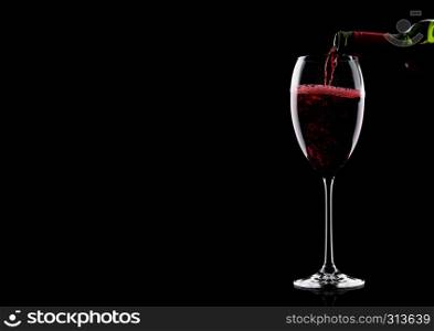 Pouring red wine from bottle to glass isolated on black background