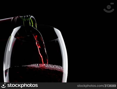 Pouring red wine from bottle to glass isolated on black background