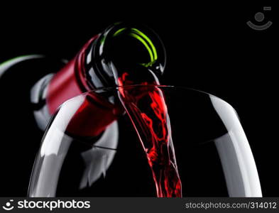 Pouring red wine from bottle to glass isolated on black background