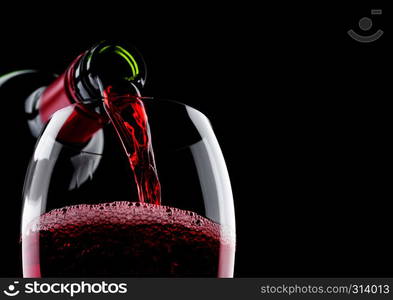 Pouring red wine from bottle to glass isolated on black background