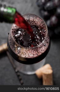 Pouring red wine from bottle to glass on black background with corks and corkscrew. Top view