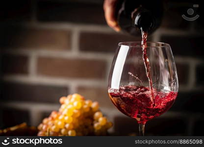 Pouring red wine into the glass on rustic dark background. Pour alcohol, winery concept.. Pouring red wine