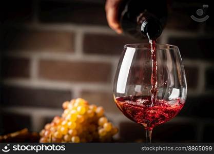 Pouring red wine into the glass on rustic dark background. Pour alcohol, winery concept.. Pouring red wine
