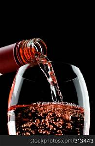 Pouring rose pink wine from bottle to glass isolated on black background