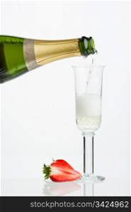 Pouring sparkling wine, split strawberry, reflection and white background.