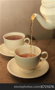 Pouring tea in classic white teacups, close up