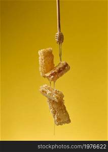 pouring transparent sweet honey from a wooden stick on a wax honeycomb. Yellow background. Food levitates