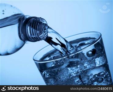pouring water from a plastic bottle into a glass with ice on a light blue background. plastic bottle and a glass with ice