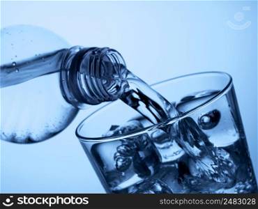 pouring  water from a plastic bottle into a glass with ice on a light blue background. plastic bottle and a glass with ice