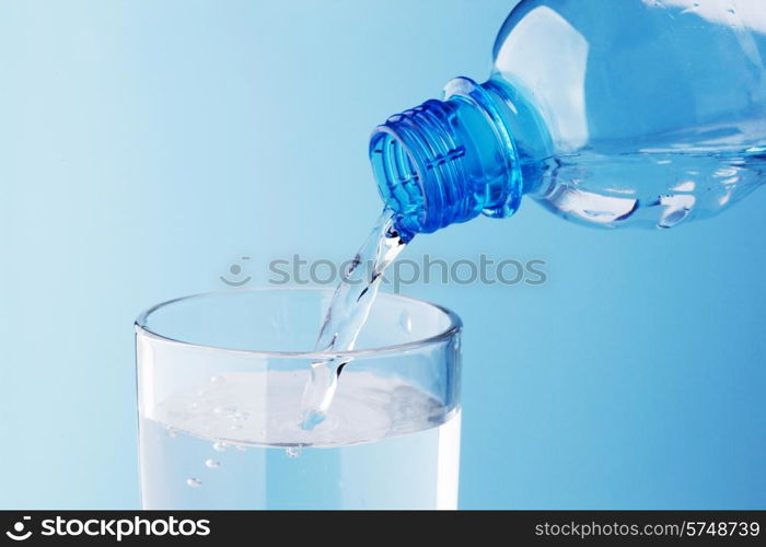 Pouring water from plastic bottle into glass on blue background. Pouring water into glass