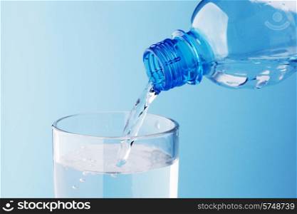 Pouring water from plastic bottle into glass on blue background. Pouring water into glass