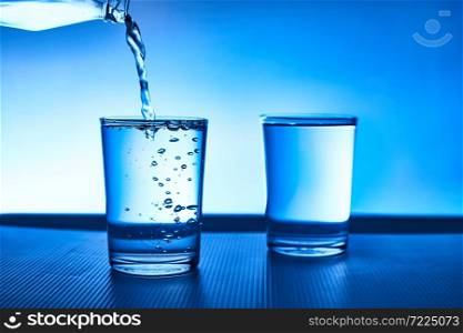 Pouring water into glass on blue background.. Pouring water into glass.
