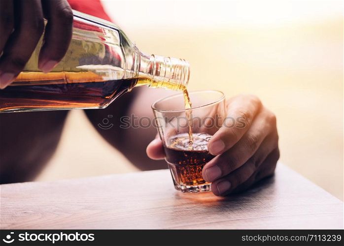 Pouring whiskey or alcohol drink from bottle to glasses on wooden background / Pour liquor