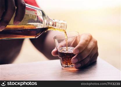 Pouring whiskey or alcohol drink from bottle to glasses on wooden background / Pour liquor