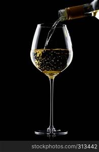 Pouring white wine from bottle to glass isolated on black background