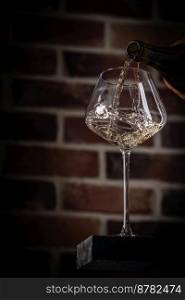 Pouring white wine into the glass against Brick wall bottom view. Pouring white wine