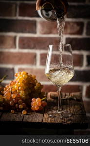 Pouring white wine into the glass on rustic dark background. Pour alcohol, winery concept.. Pouring white wine