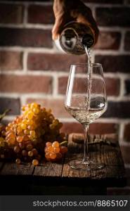 Pouring white wine into the glass on rustic dark background. Pour alcohol, winery concept.. Pouring white wine