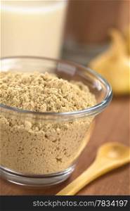 Powdered Maca or Peruvian ginseng (lat. Lepidium meyenii) in glass bowl with milk, chocolate drink and maca roots in the back (Selective Focus, Focus one third into the maca powder). Maca Powder (Flour)