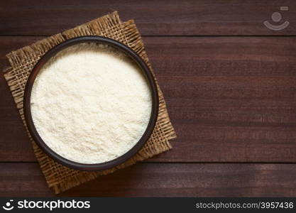 Powdered or dried milk in bowl, photographed overhead on dark wood with natural light (Selective Focus, Focus on the top of the milk powder)