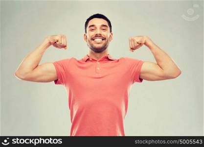 power, fitness, strength, sport and people concept - happy smiling young smiling man showing biceps over gray background. smiling man showing biceps over gray background