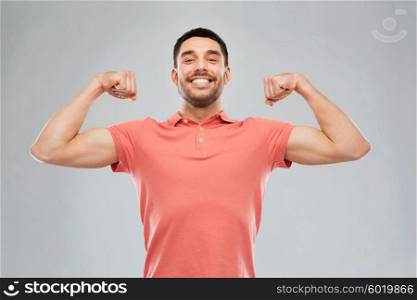 power, fitness, strength, sport and people concept - happy smiling young smiling man showing biceps over gray background