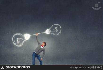 Power in good idea. Confident man lifting above head barbell with light bulbs