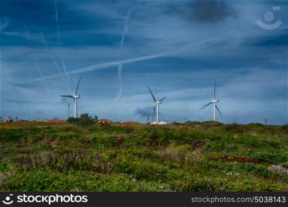 Power wind mills in a green hill against hazy sky in Portugal.