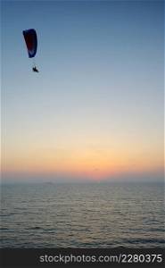 Powered paraglider flying over the sea at sunset sky background. Powered paragliding