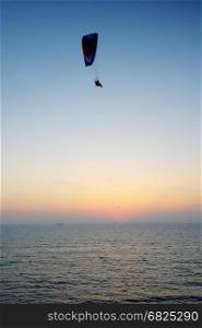 Powered paraglider flying over the sea at sunset sky background. Powered paragliding