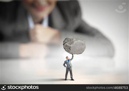 Powerful businessman. Businesswoman looking at miniature of businessman lifting stone above head