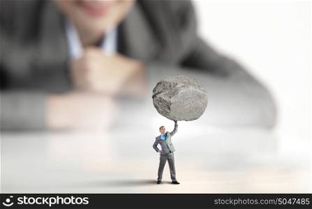 Powerful businessman. Businesswoman looking at miniature of businessman lifting stone above head