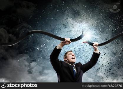 Powerful businessman. Young businessman tearing electricity cable with hands