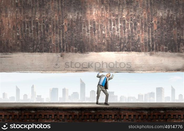 Powerful businessman. Young powerful businessman lifting brick wall above head