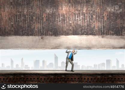 Powerful businessman. Young powerful businessman lifting brick wall above head