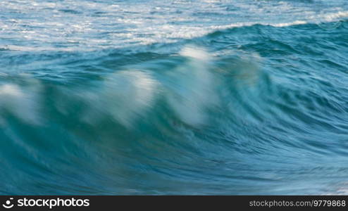 Powerful large turquoise colored waves crashing at Sennen Cove in Cornwall during late sunset