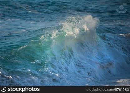 Powerful large turquoise colored waves crashing at Sennen Cove in Cornwall during late sunset