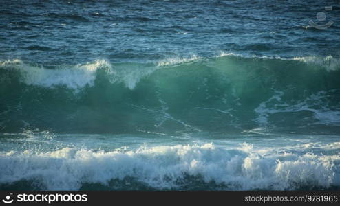 Powerful large turquoise colored waves crashing at Sennen Cove in Cornwall during late sunset