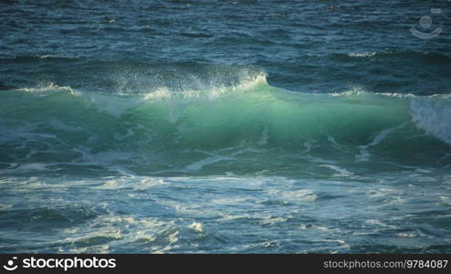 Powerful large turquoise colored waves crashing at Sennen Cove in Cornwall during late sunset