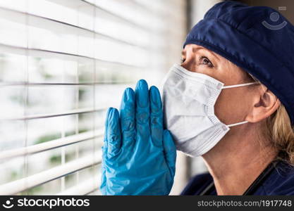 Prayerful Stressed Female Doctor or Nurse On Break At Window Wearing Medical Face Mask.