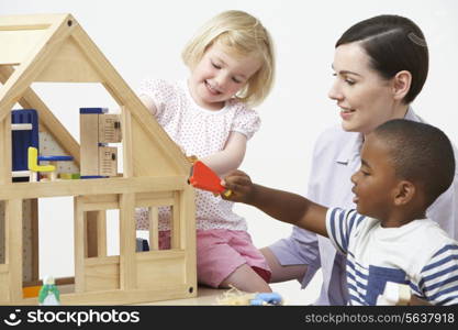 Pre-School Teacher And Pupils Playing With Wooden House