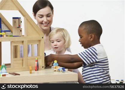 Pre-School Teacher And Pupils Playing With Wooden House