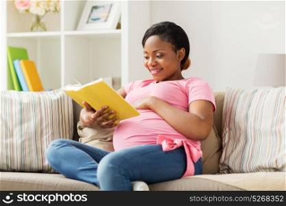 pregnancy and leisure concept - smiling pregnant african american woman reading book at home. happy pregnant african woman reading book at home