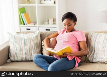 pregnancy and leisure concept - smiling pregnant african american woman reading book at home. happy pregnant african woman reading book at home